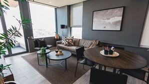 A modern living room with a sofa, two round tables, and a large window with a city view. - Umhlanga Arch Luxury Holiday or Work with Sea View (Durban)