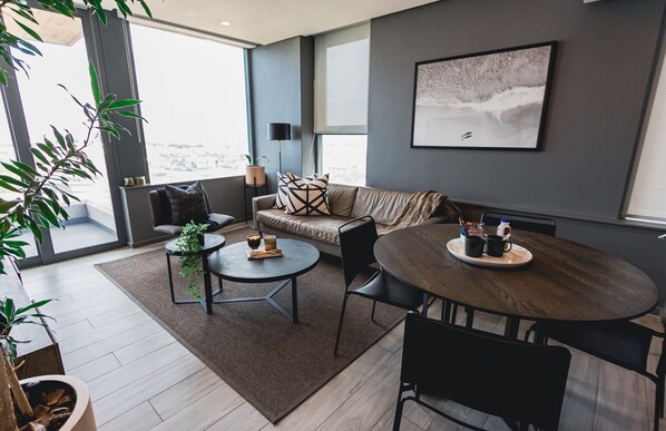 Una sala de estar moderna con un sofá, dos mesas redondas y un ventanal con vistas a la ciudad.