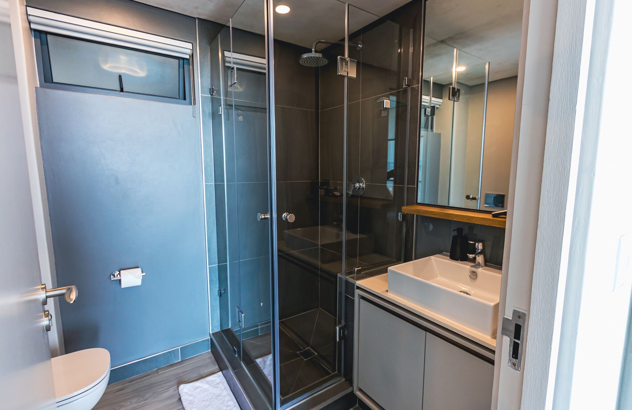 Et moderne badeværelse med en bruseniche, en hvid vask og et toilet.
