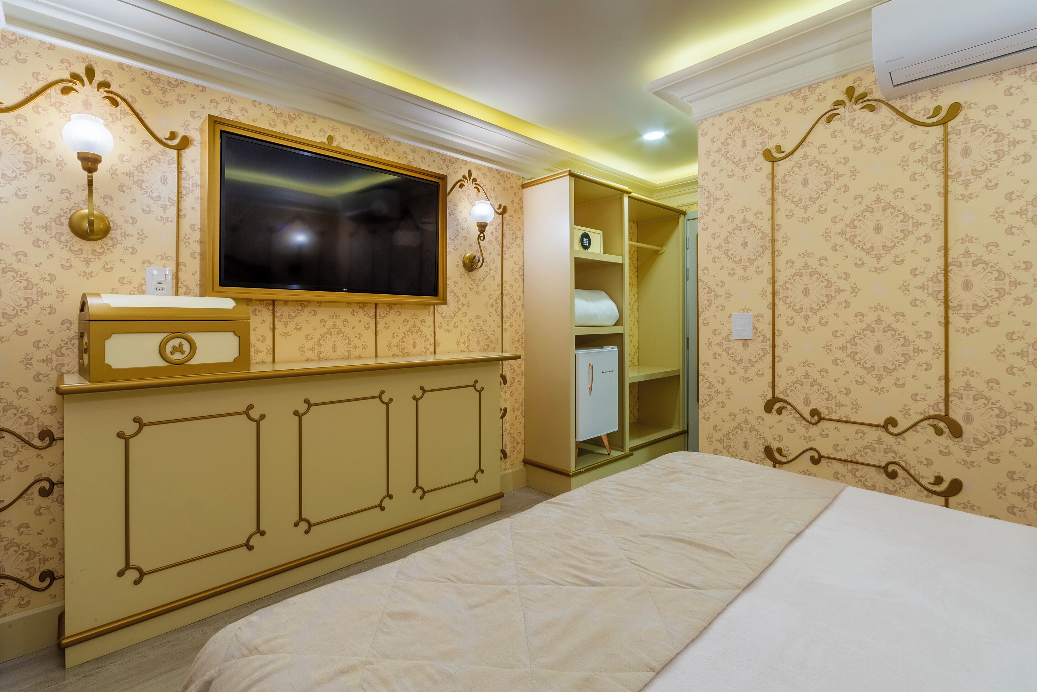 A bedroom with a bed, a TV mounted on the wall, a wardrobe, and a bedside table.