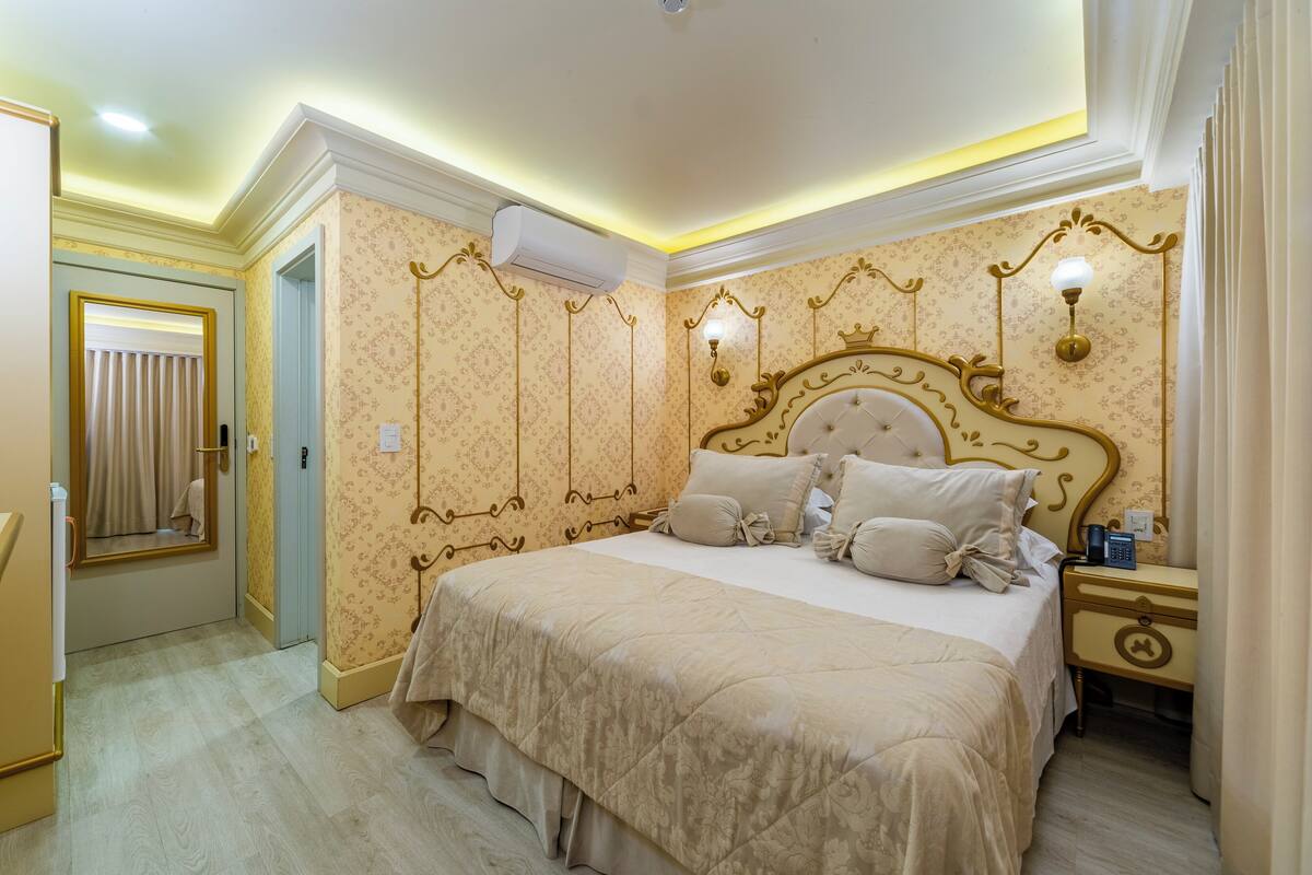 A bedroom with a large bed, a nightstand, a wall-mounted lamp, and an air conditioning unit.