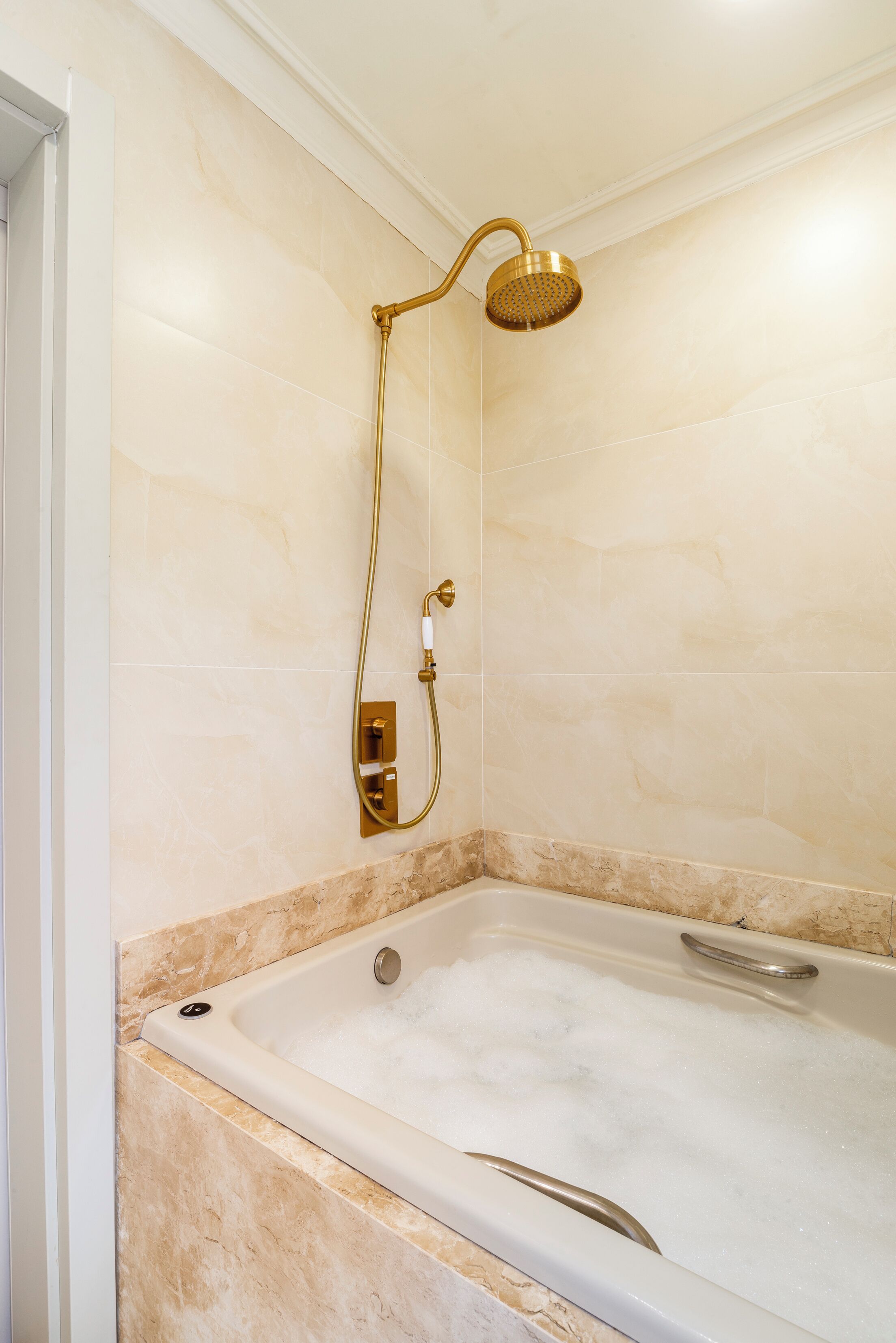 A bathroom with a bathtub, a showerhead, and a control panel.