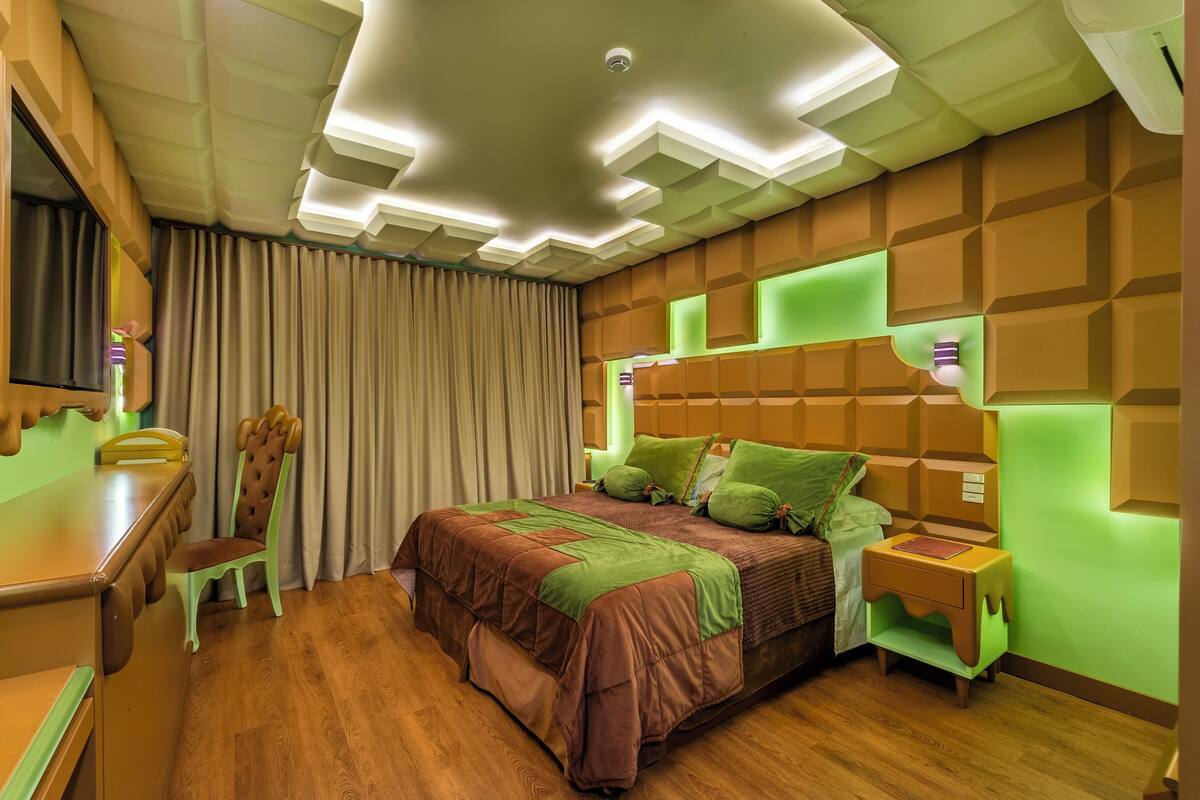 A modern bedroom with a wooden desk, a chair, a bed with green bedding, and a nightstand.