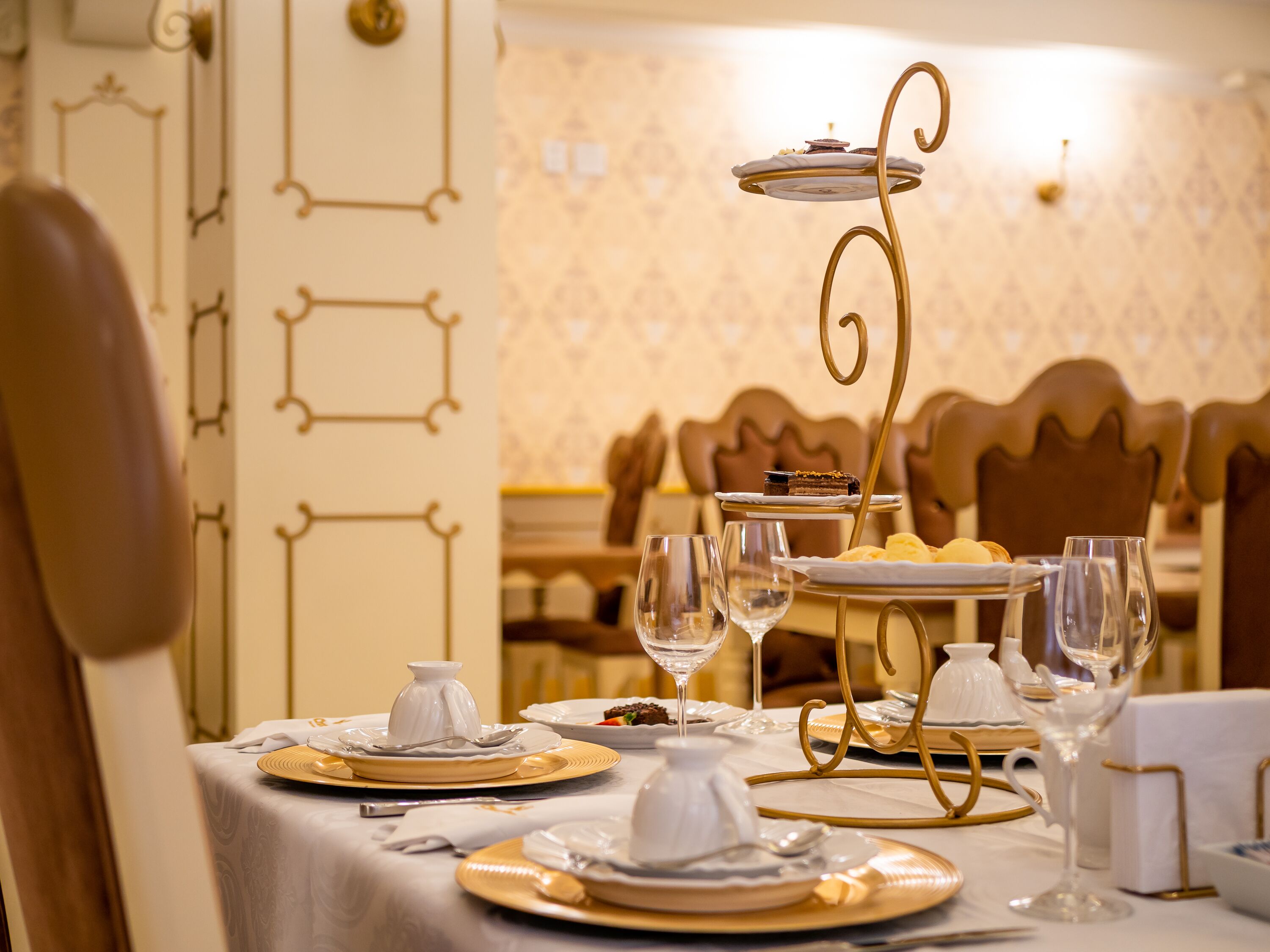 Una mesa de comedor servida con platos, vasos y un pastelero escalonado en un restaurante.