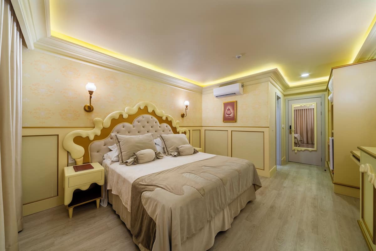 A bedroom with a large bed, bedside tables, a nightstand, an air conditioning unit, and a door with a mirror.