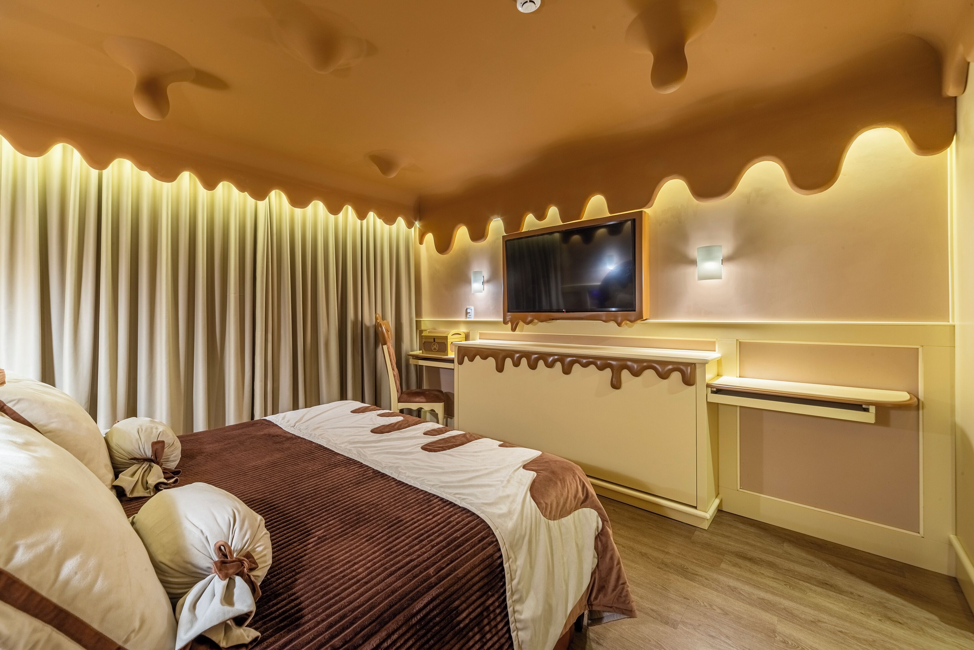 A hotel room with a bed, curtains, a TV, a desk, and a chair.