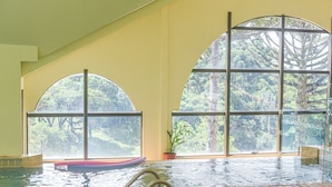 An indoor swimming pool with large arched windows offering views of a forested area. - Chocoland Hotel Gramado (Gramado)
