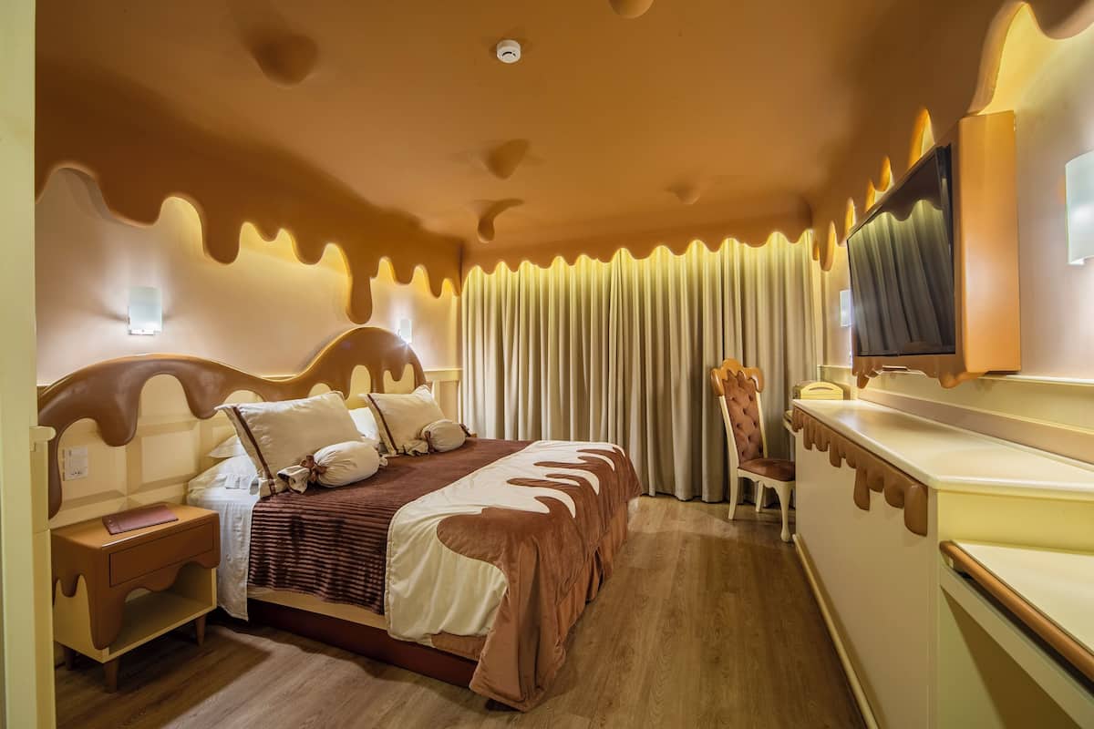 A hotel room with a bed, a TV, curtains, a chair, and a bedside table.