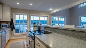 A modern kitchen with granite countertops, white cabinetry, and large windows offering views of the outdoors.