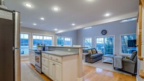 A spacious kitchen with a central island, a dining area with a sofa and coffee table, and large windows offering views of the outdoors.