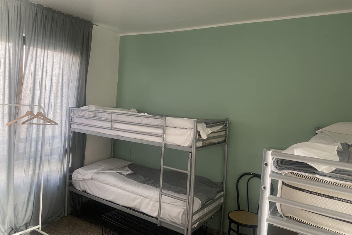 Une chambre avec un lit superposé doté d’une structure en métal, d’un porte-manteau en bois et d’une chaise.