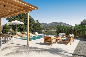 A pool area with lounge chairs, a pergola, and a view of mountains.