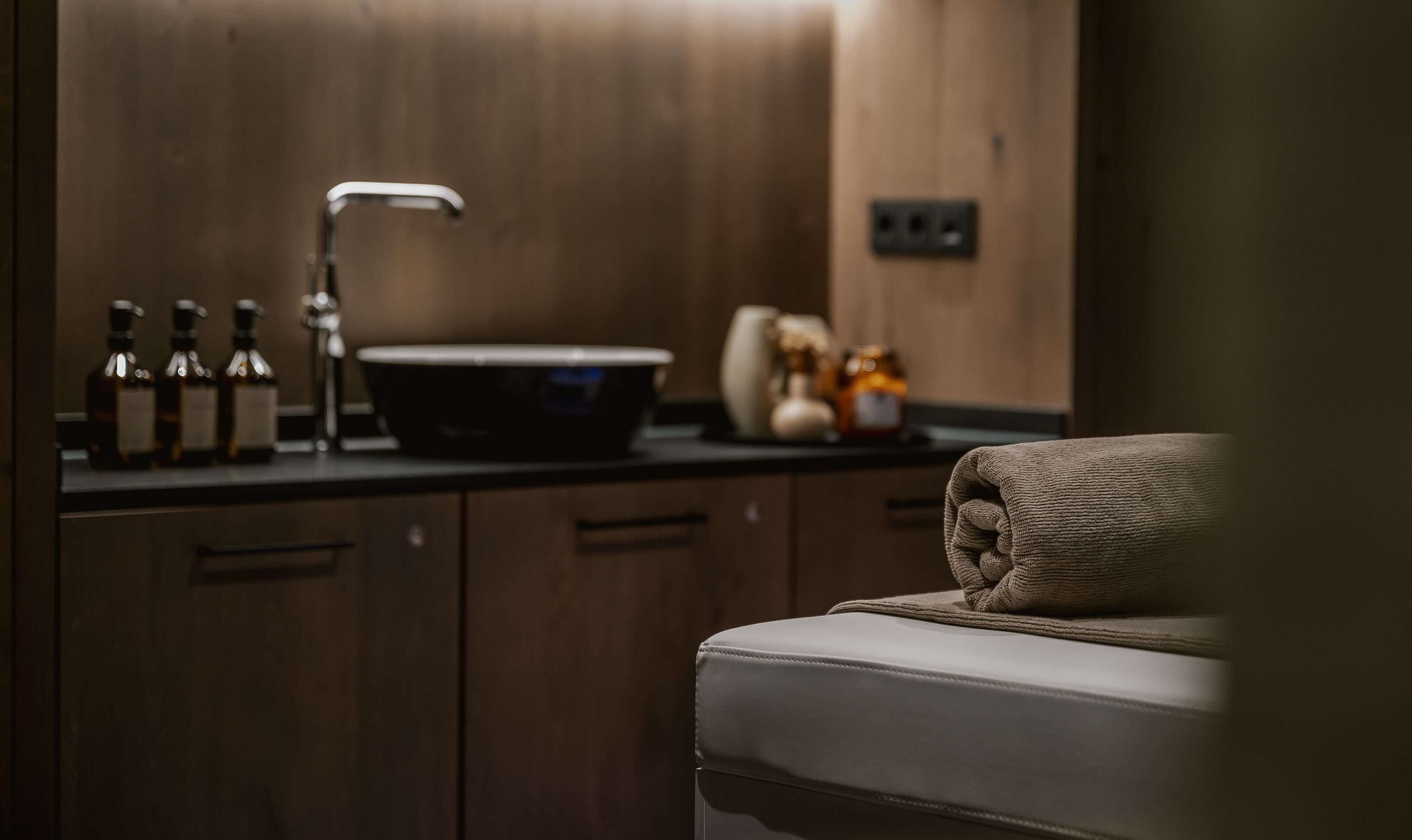 Uma casa de banho moderna com toucador de madeira, lavatório preto e toalha sobre um banco estofado.