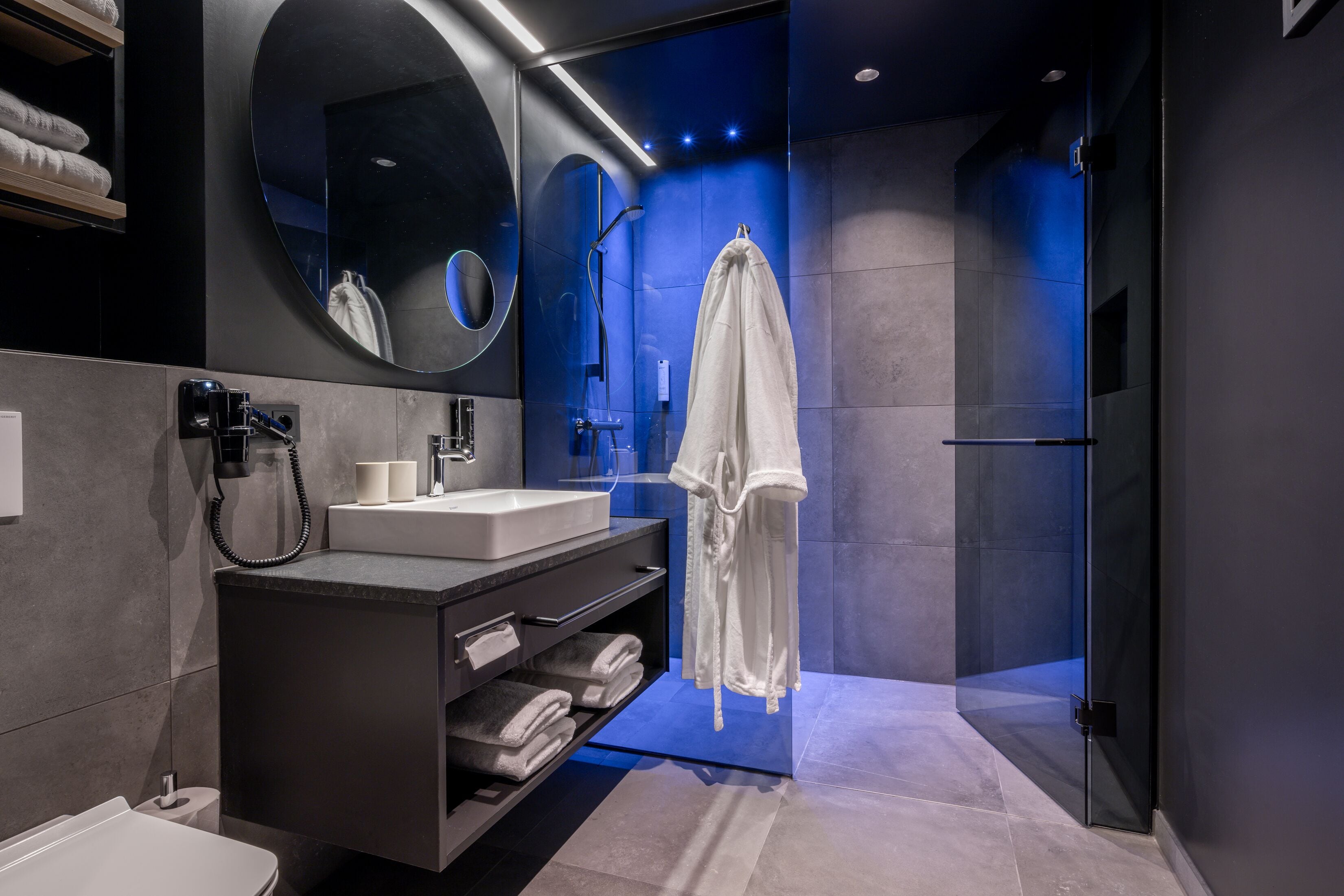A modern bathroom with a large mirror, a vanity with a sink, and a glass shower enclosure.