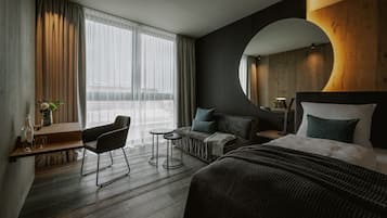Une chambre d’hôtel moderne avec un grand lit, un canapé, un bureau avec une chaise et une petite table.
