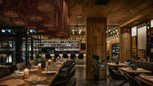 Un restaurant doté d’une longue table en bois, dressée pour le dîner, d’un bar avec des étagères remplies de bouteilles, et d’un intérieur chaleureux, tout en bois.