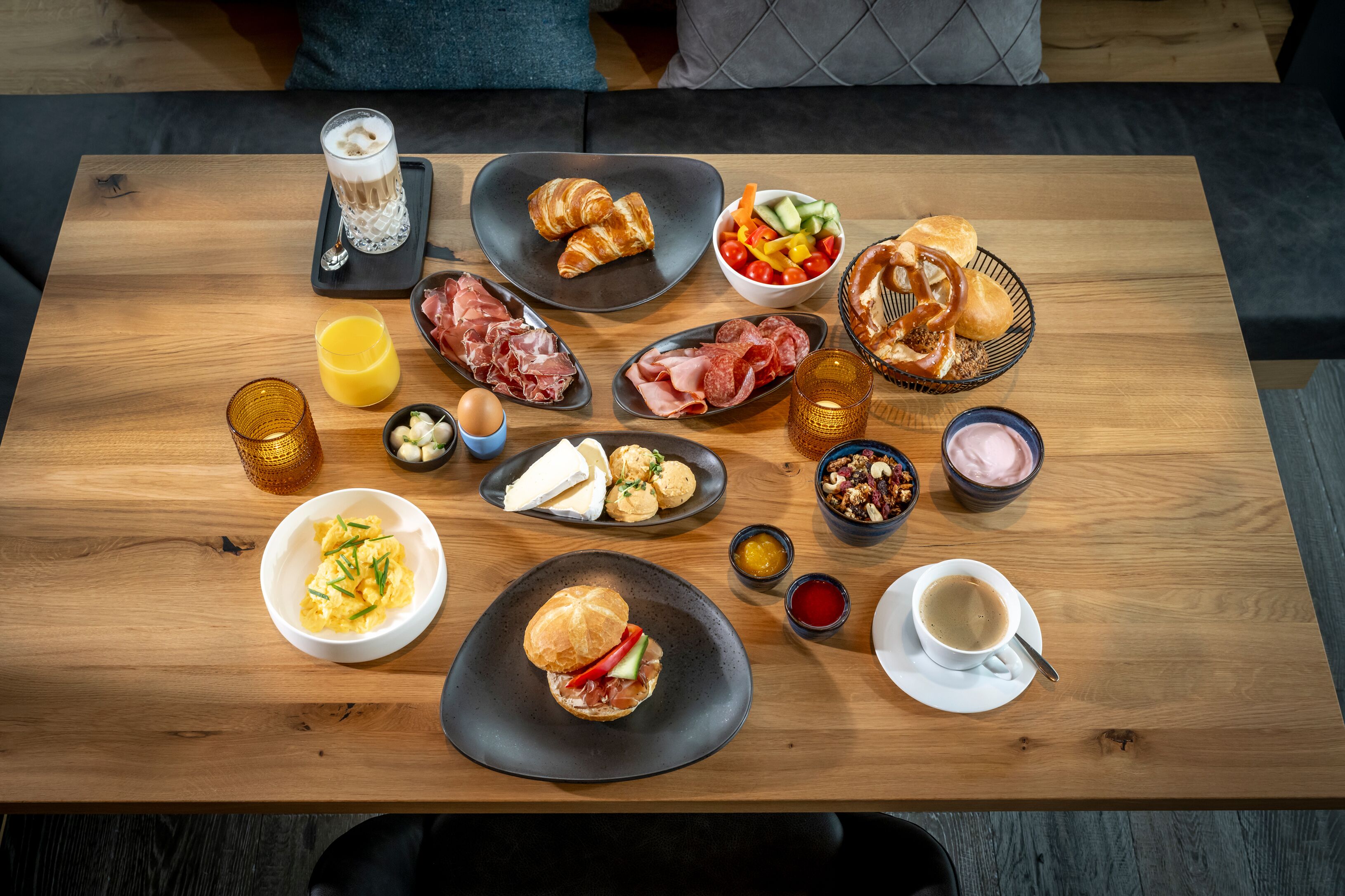 Une table en bois sur laquelle sont disposés divers aliments pour le petit-déjeuner, notamment des croissants, de la charcuterie, des œufs et des boissons.