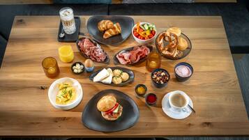 Une table en bois sur laquelle sont disposés divers aliments pour le petit-déjeuner, notamment des croissants, de la charcuterie, des œufs et des boissons.