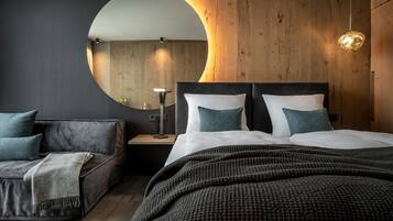 A modern bedroom with a large bed, a round mirror, a wooden accent wall, and a side table with a lamp.