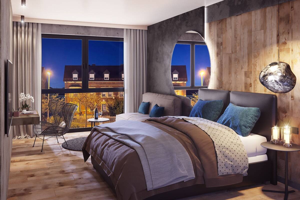 Ein modernes Schlafzimmer mit einem großen Bett, einem Schreibtisch und einem Stuhl. Große Fenster bieten Blick auf umliegende Gebäude.