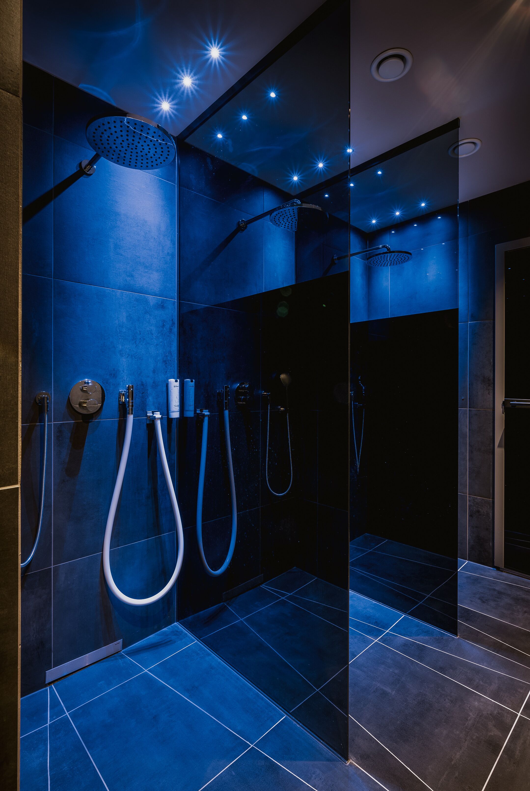 A modern bathroom with blue-tiled walls, a glass shower enclosure, and multiple showerheads.