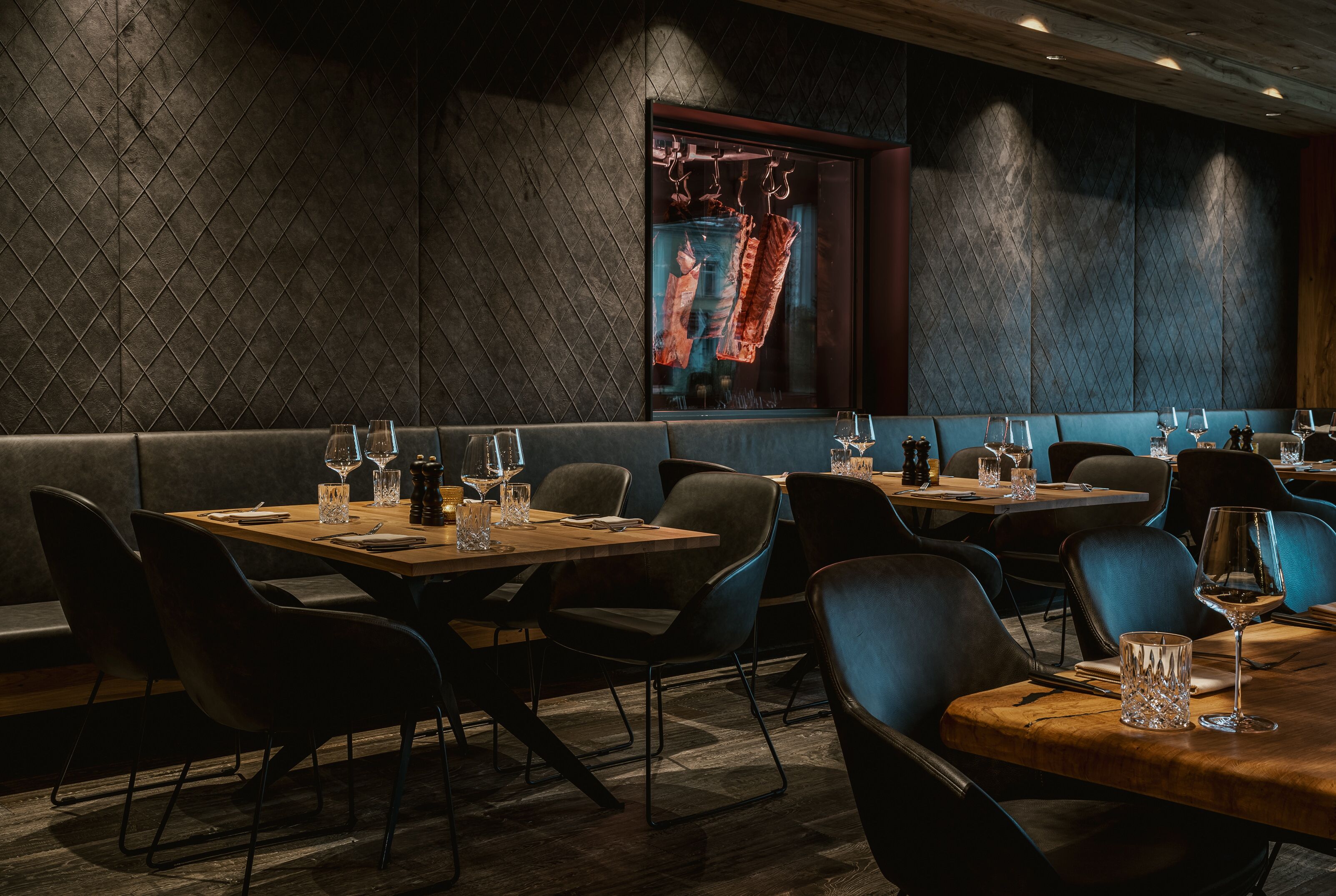 A restaurant with dark, patterned walls, wooden tables, and black chairs.