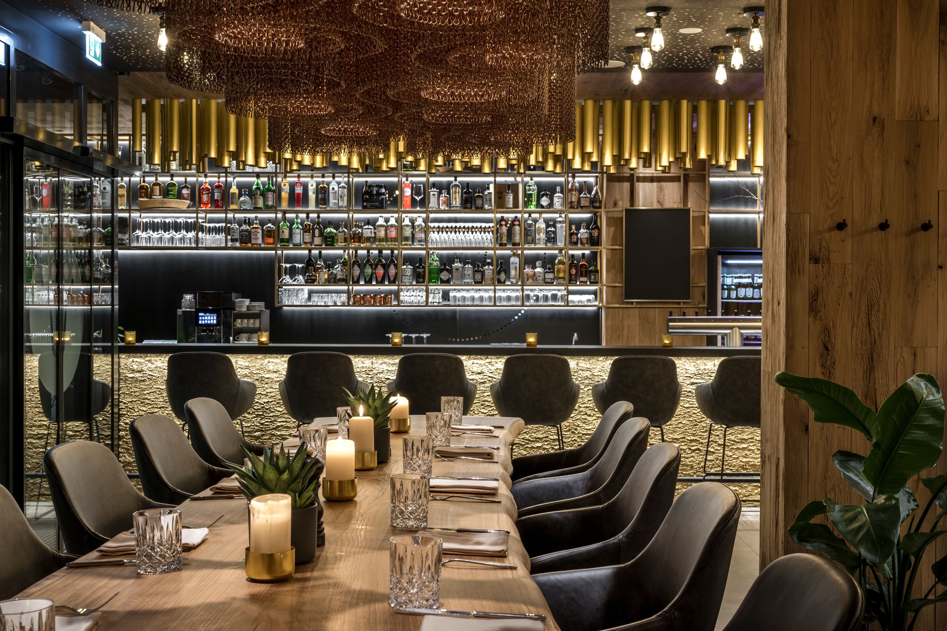 A bar area with a long counter, shelves of bottles, and a seating area with tables and chairs.