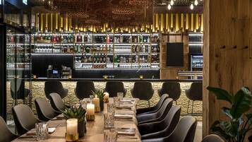 A bar area with a long counter, shelves of bottles, and a seating area with tables and chairs.