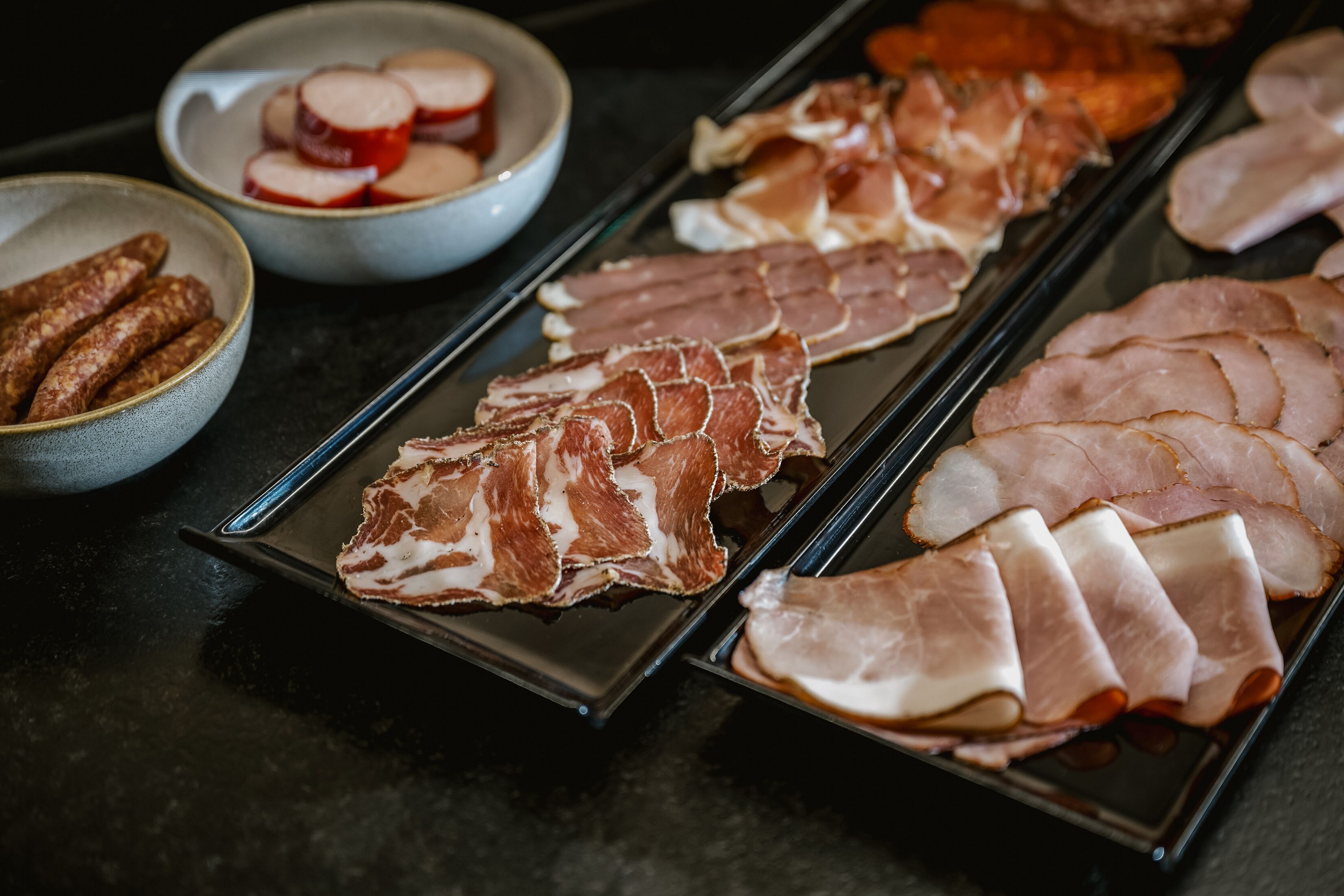 Una variedad de carnes cortadas en un plato, incluyendo jamón y salchichas.