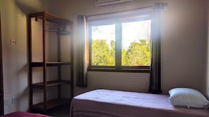 Una habitación con dos camas, un estante de madera y una ventana con vista a árboles.