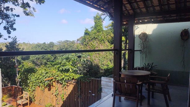 Un balcón con mesa y sillas de madera, rodeado de plantas en macetas y vistas de vegetación exuberante.