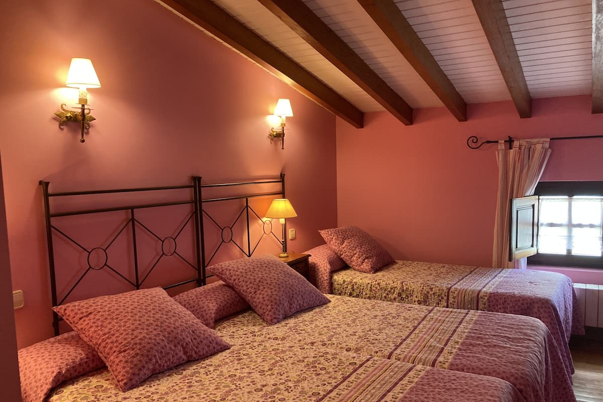 Une chambre avec deux lits, chacun agrémenté de draps et d’oreillers assortis à motifs floraux. Des lampes murales sont fixées de chaque côté des lits.