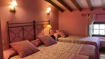 A room with two beds, each with floral-patterned bedding and matching pillows. There are wall-mounted lamps on either side of the beds.