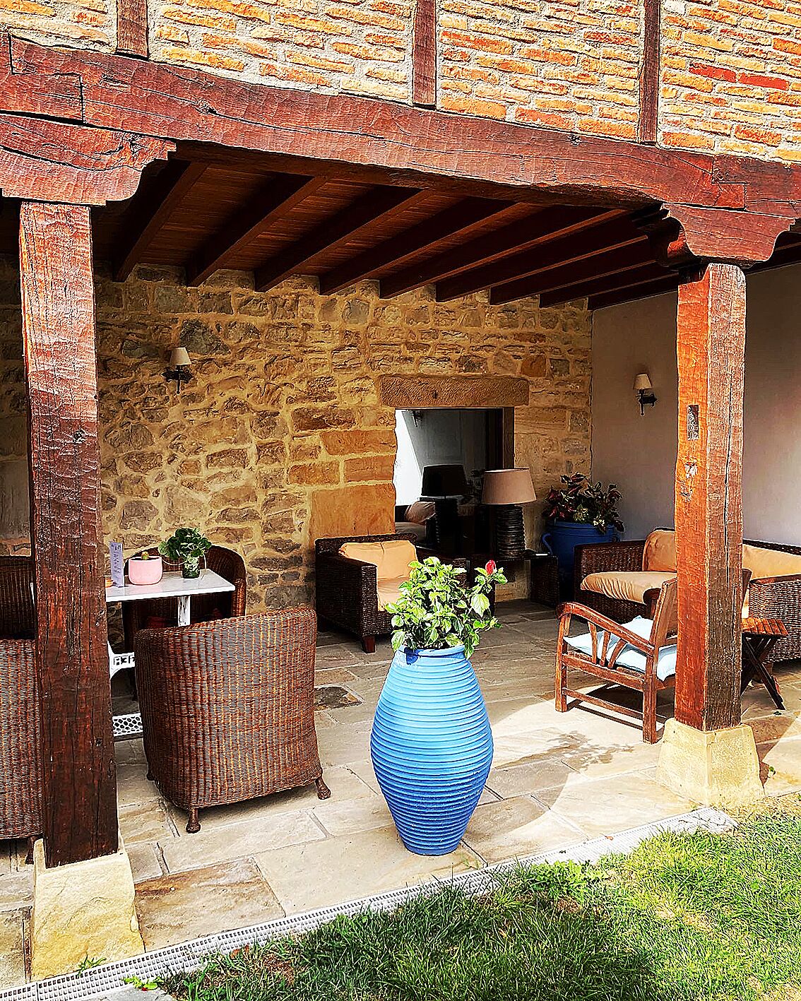 Un patio al aire libre con paredes de piedra, muebles de mimbre y un gran jarro azul con plantas.