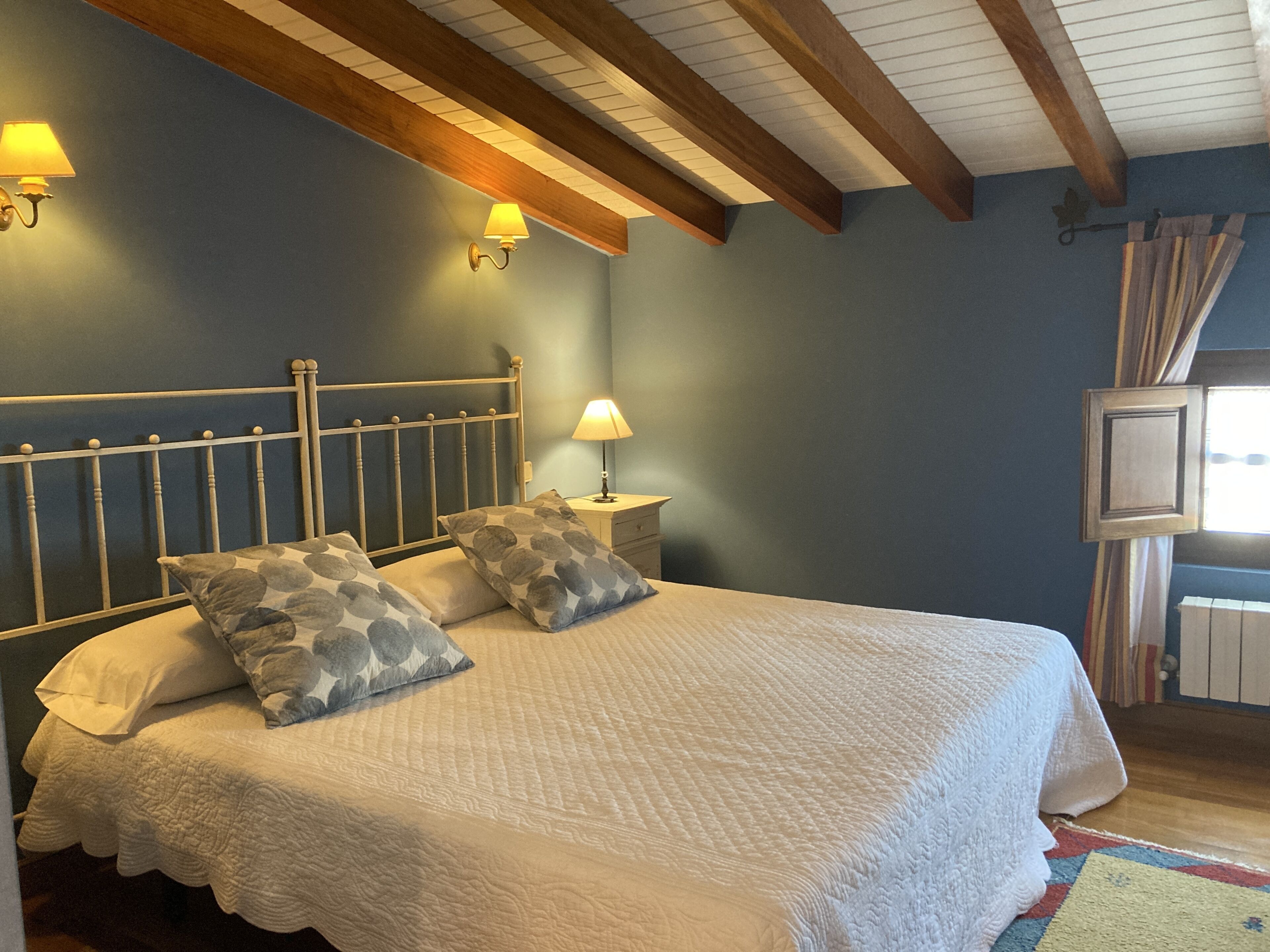 A bedroom with a bed, two wall-mounted lamps, a nightstand, and a window with curtains.