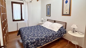 A bedroom with a wooden bed, a small bedside table, a window with curtains, and a ceiling fan. - Posada La Casona de Los Güelitos (Santillana del Mar)