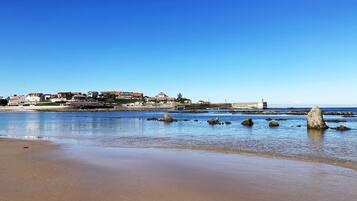 A coastal town with buildings along the shore, a lighthouse, and rocky outcrops in the water.