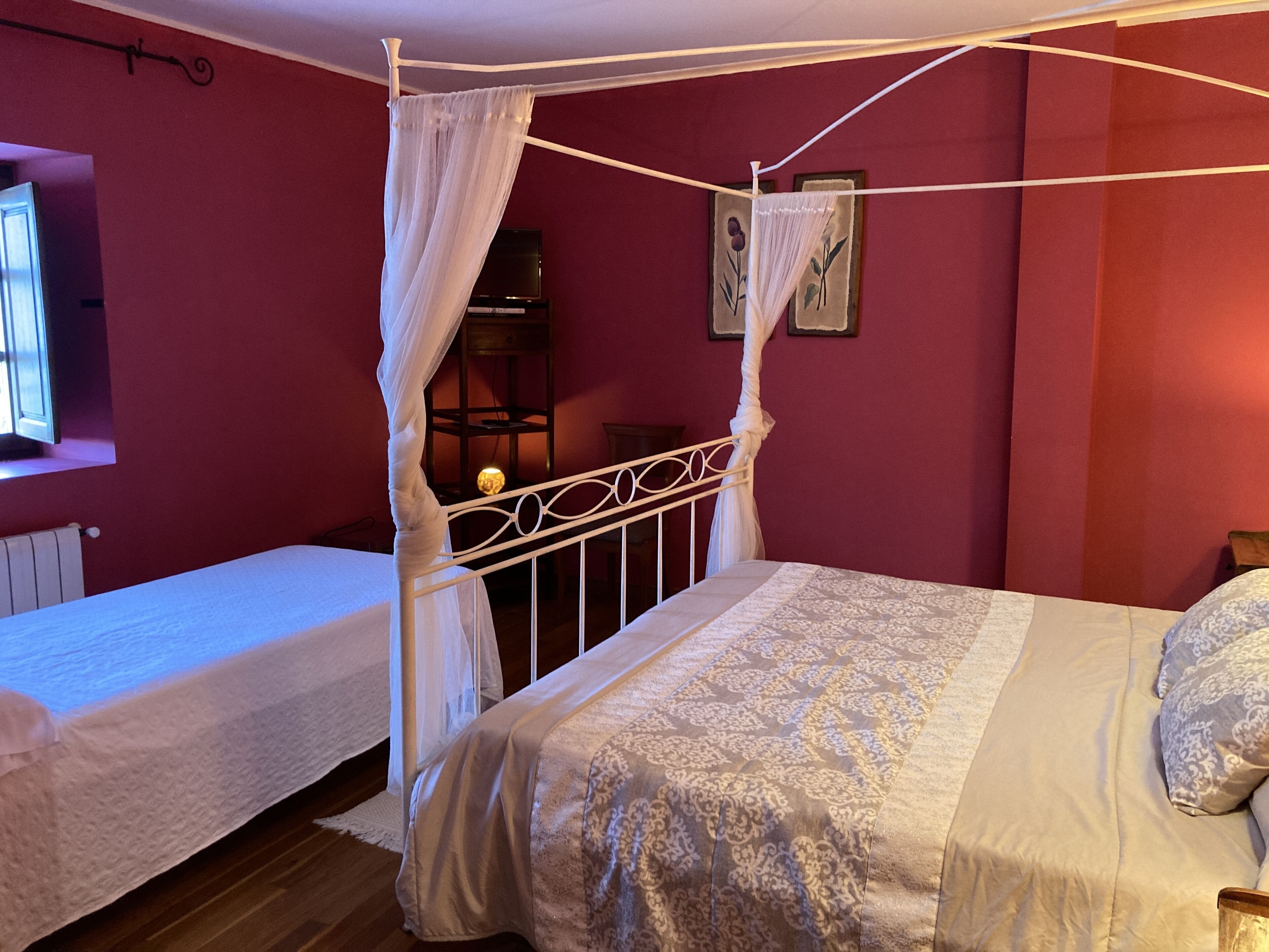 Un dormitorio con una cama con dosel, una cama individual más pequeña y una mesita de noche con una lámpara.