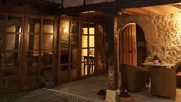 A traditional half-timbered building with a stone archway entrance, wooden shutters, and a stone pathway leading to a seating area with potted plants. - Posada La Casona de Los Güelitos (Santillana del Mar)