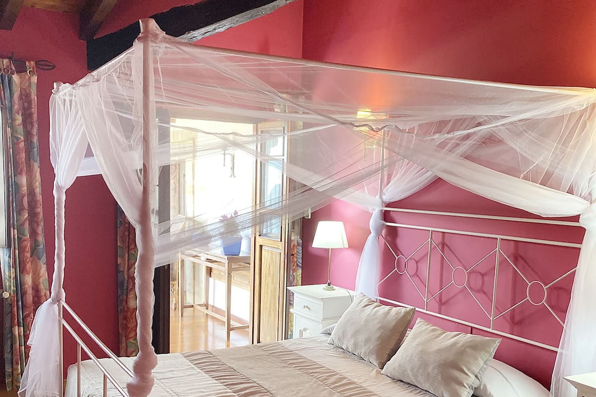 Une chambre à coucher avec un lit à baldaquin, une table de chevet, une lampe et une fenêtre avec des rideaux.