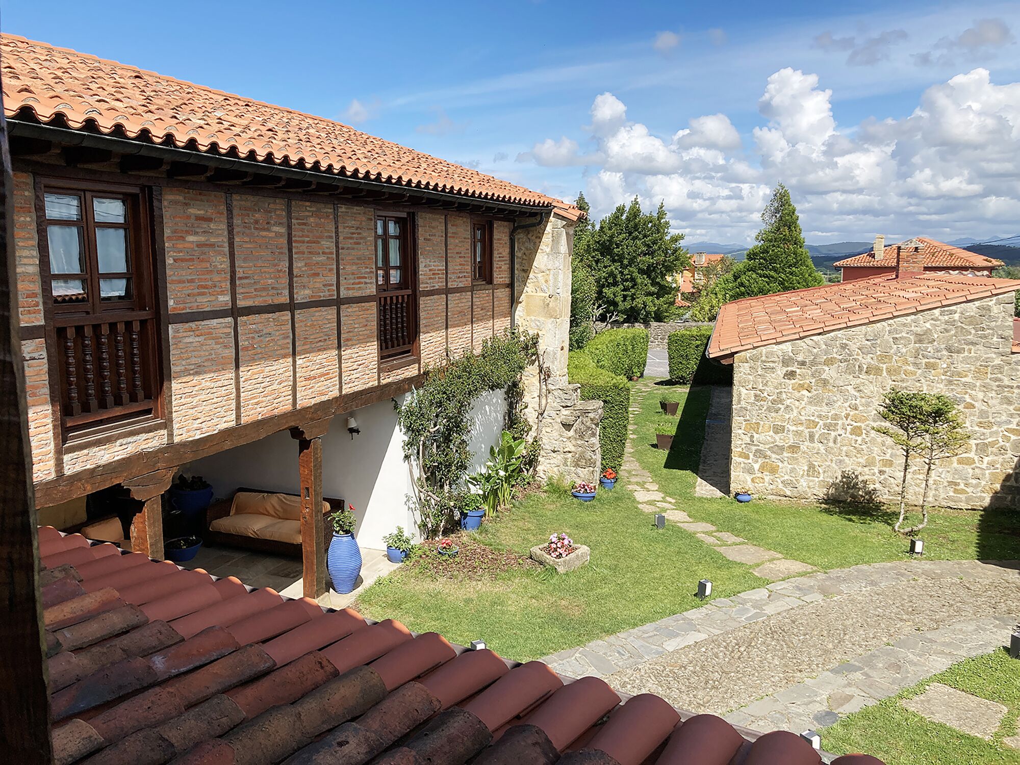 A traditional half-timbered house with a tiled roof, a stone wall, and a small garden with potted plants.