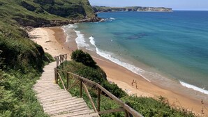 A coastal beach with a wooden staircase leading down to the shore, surrounded by greenery and cliffs. - Posada La Casona de Los Güelitos (Santillana del Mar)