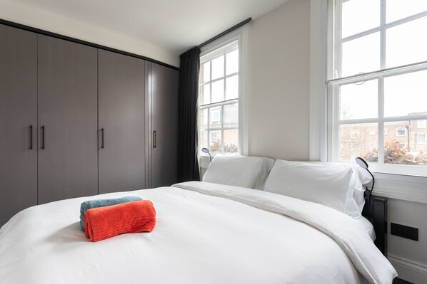 Un dormitorio con cama, armario gris y ventana con cortinas.