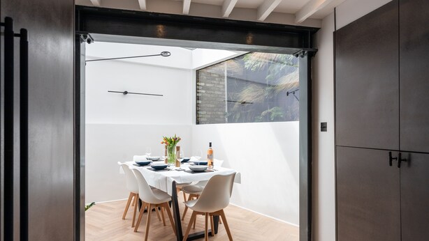 A dining area with a round table set for four, white chairs, and a vase with flowers. - Stunning townhouse with large roof terrace (London)