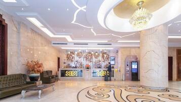 A hotel lobby with a reception desk, seating area, and a chandelier.