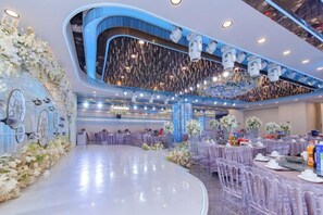 A spacious indoor venue with tiered seating, decorative floral arrangements, and a modern ceiling design. - Guanghe International Hotel (Yueyang)