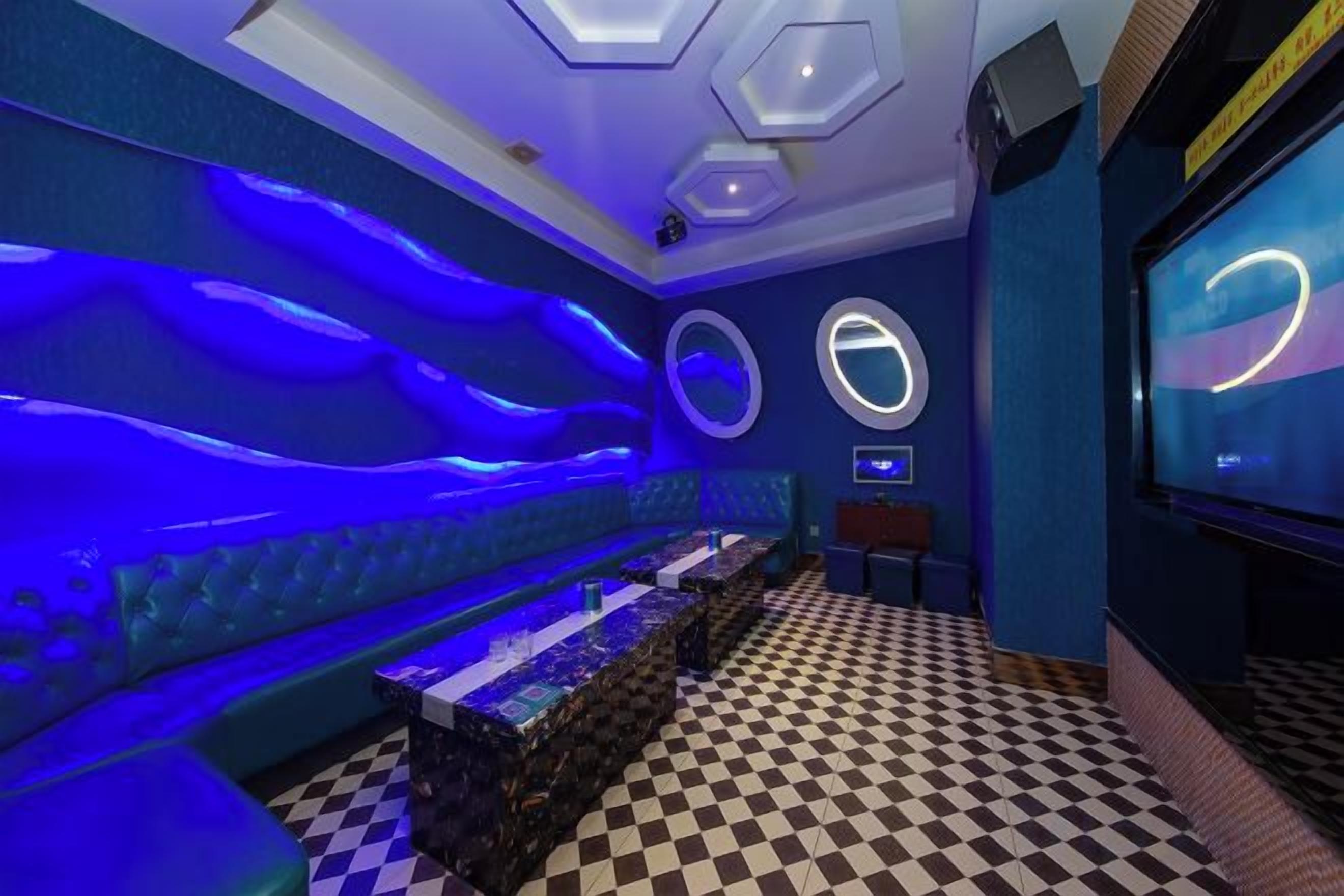 A room with a checkered floor, a blue-lit seating area, and a television screen.