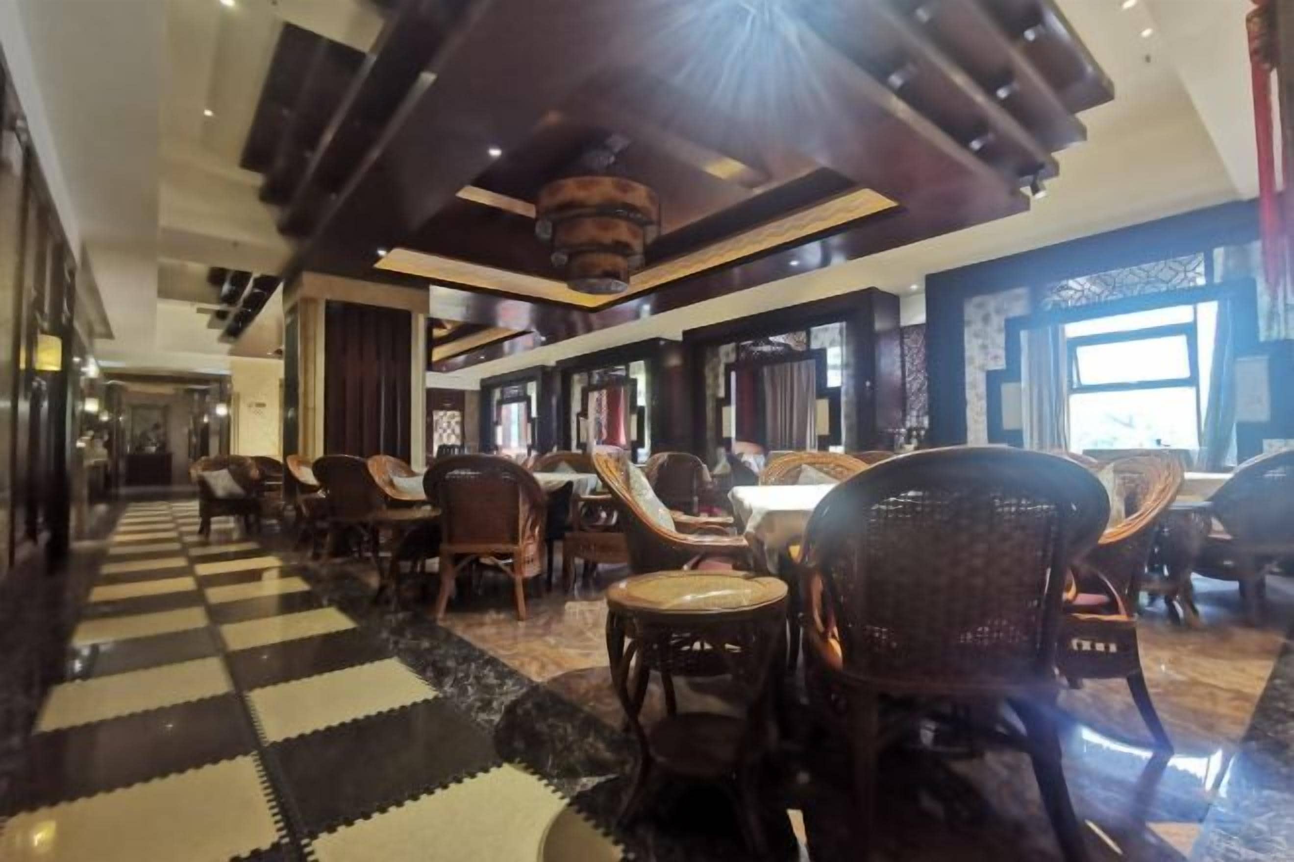 A hotel lobby with a checkered floor, multiple seating areas, and a large window providing natural light.