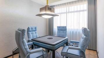 Una habitación moderna con una mesa central y cuatro sillas azules, un proyector en el techo y un ventanal con cortinas.