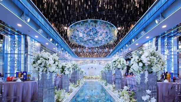 A grand hall with a central reflective pool, flanked by ornate columns and floral arrangements.